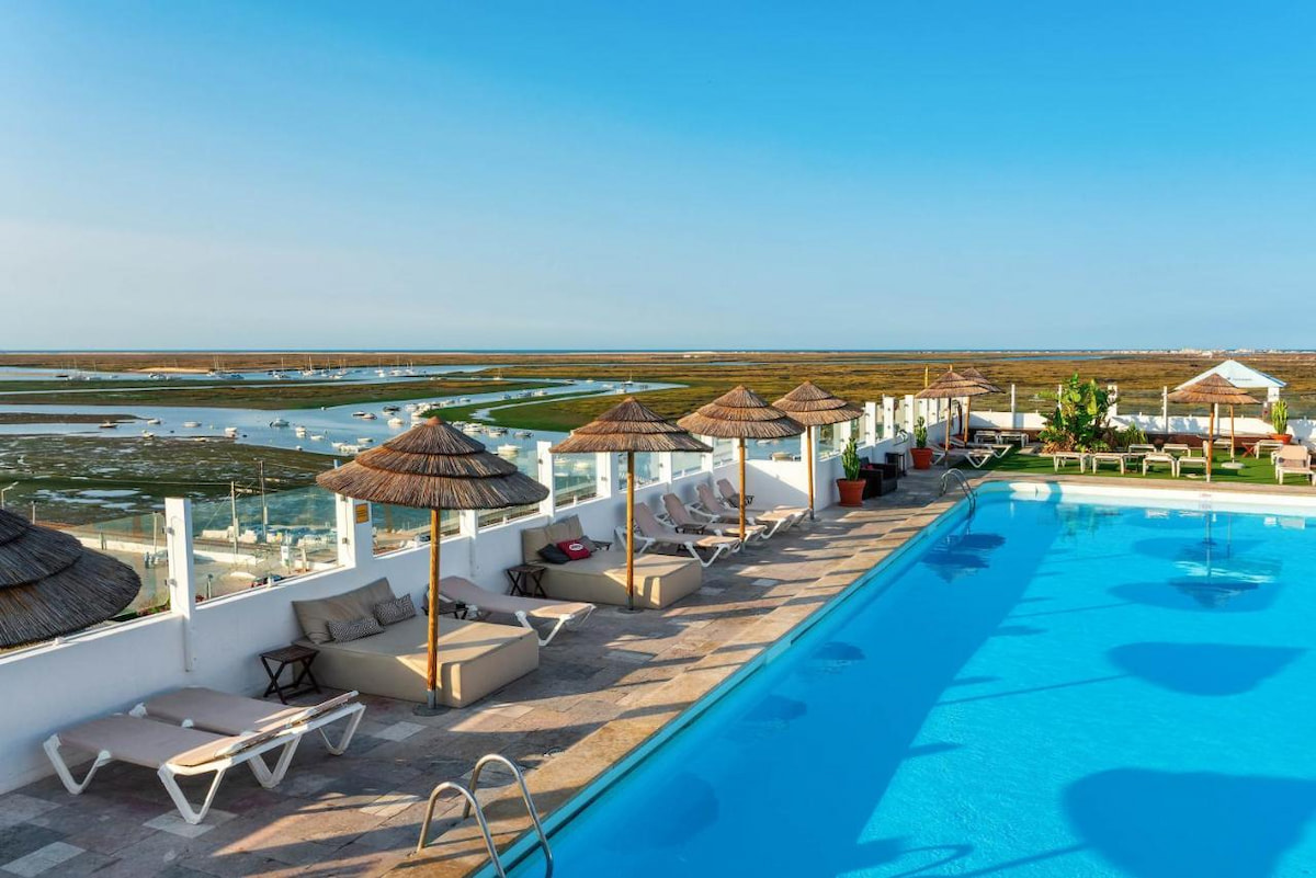 large outdoor pool with sun loungers and umbrellas overlook the natural reserve near best town in Algarve Faro