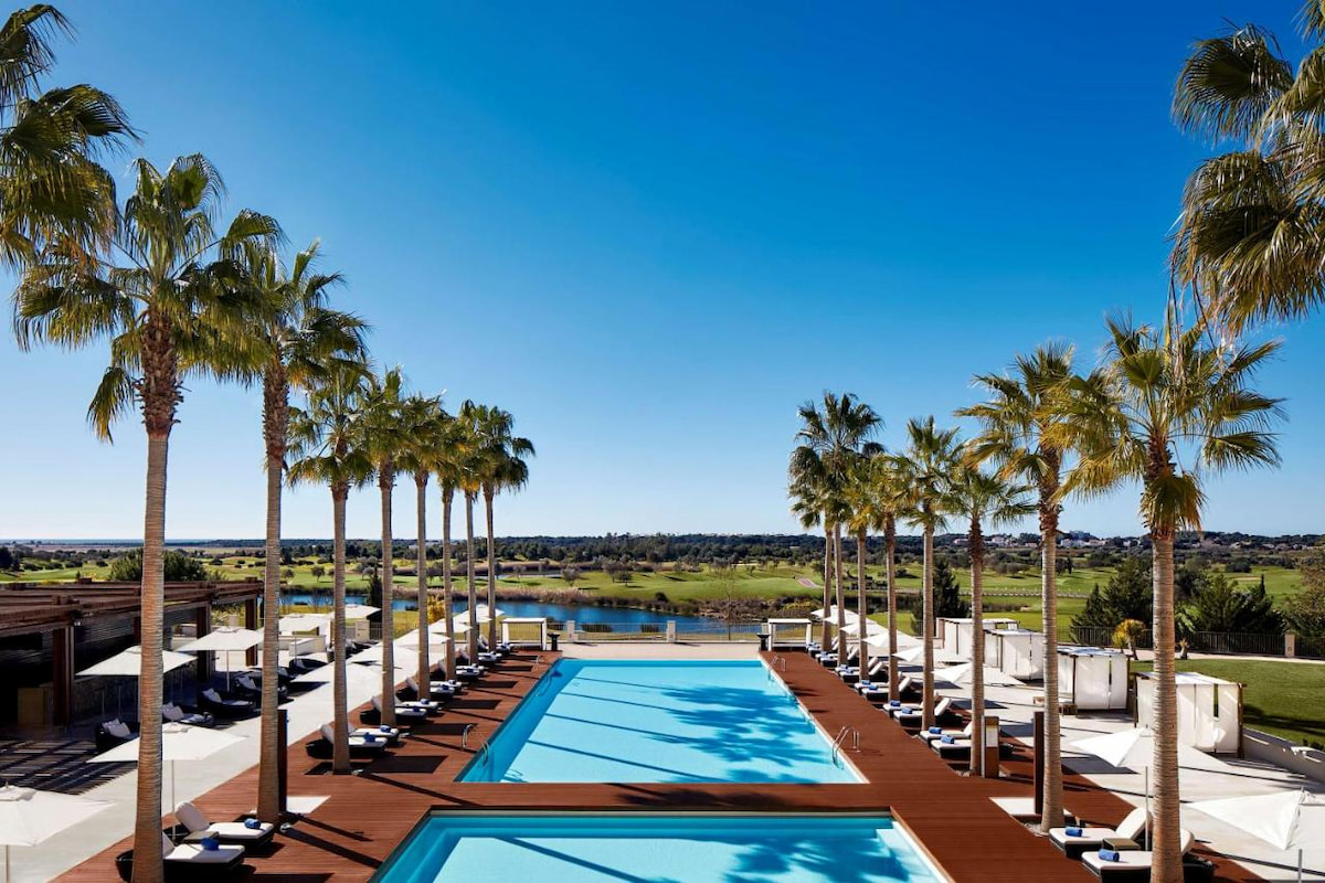 boutique hotel outdoor area with two pools, white loungers and lined with palm trees in one of the best places in Algarve for luxury travellers