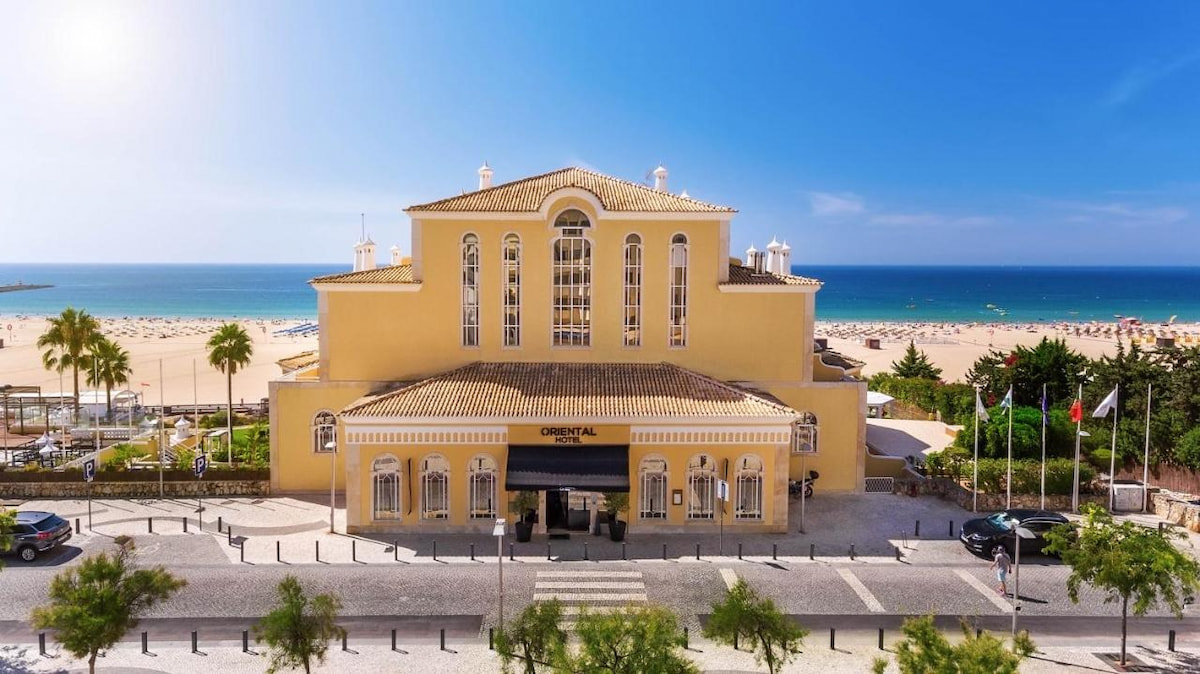 beachfront resort in Algarve best town with large yellow building sitting on the coastline with sandy beach and ocean in the distance with blue sky