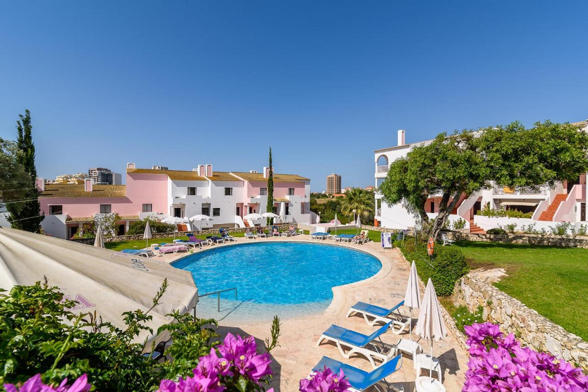 aparthotel sits behind an outdoor pool with pink flowers on a sunny day on where to stay Algarve Coast for shopping