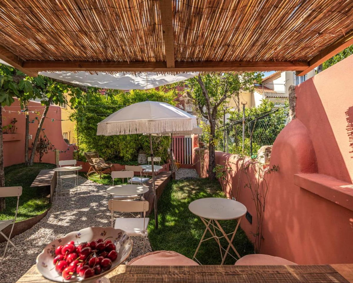 lush green outdoor space at Estrela Lisbon hotel with pink wall and furniture under a white umbrella