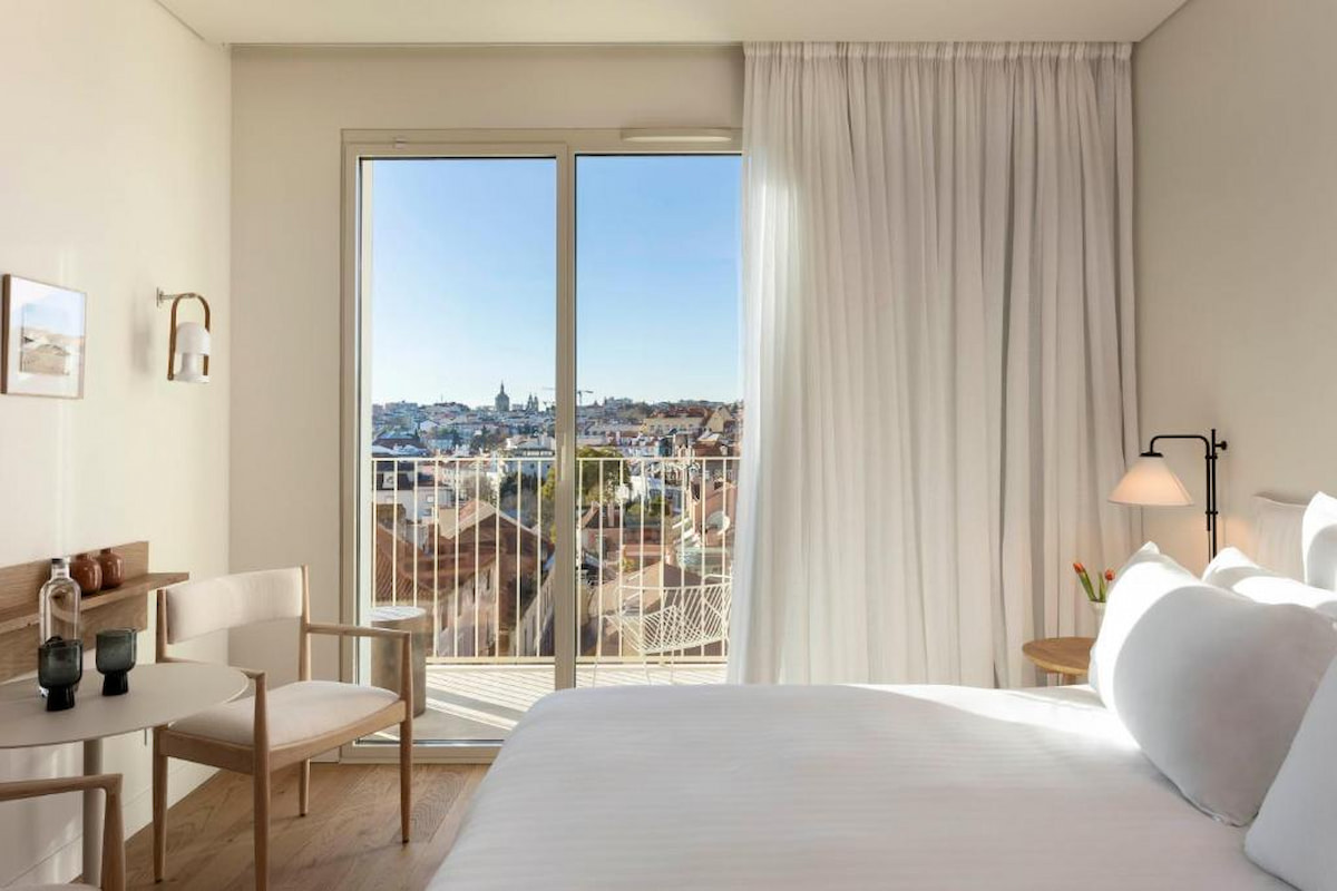 sunny place to stay in Lisbon with white linen bed, wood chair and large window overlooking Bairro Alto