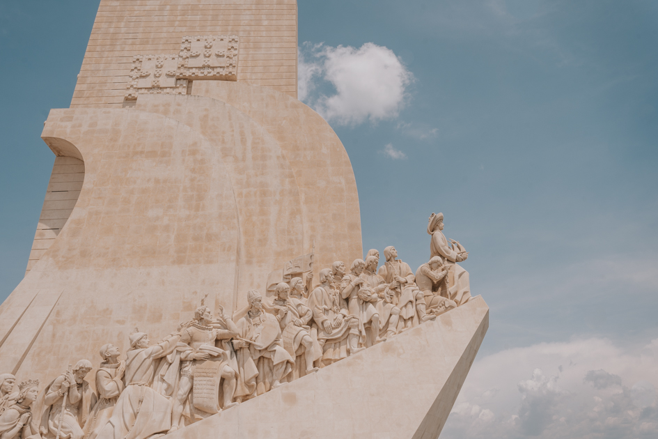 a close up of the white stone Monument to the Discoveries with detailed human statues climbing up into a blue sky 