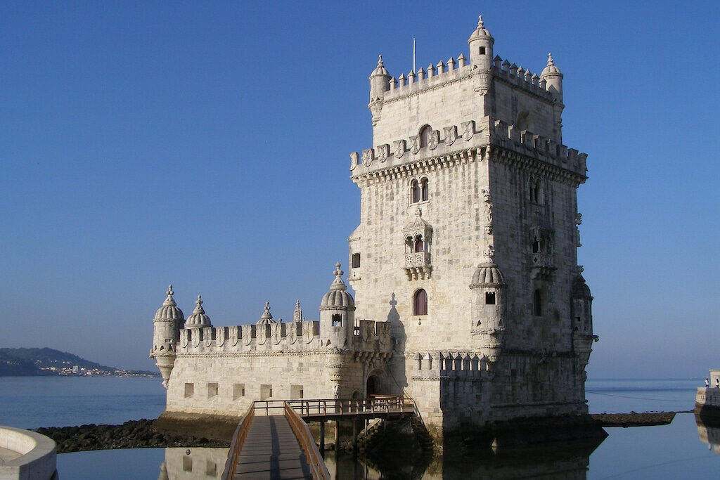 square white stone tower sits on the edge of the ocean in Lisbon, Portugal