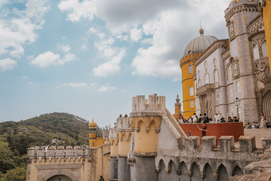 a yellow, red and white ornate palace tops a hill on a partly cloudy day in Sintra the top day trip from Lisbon