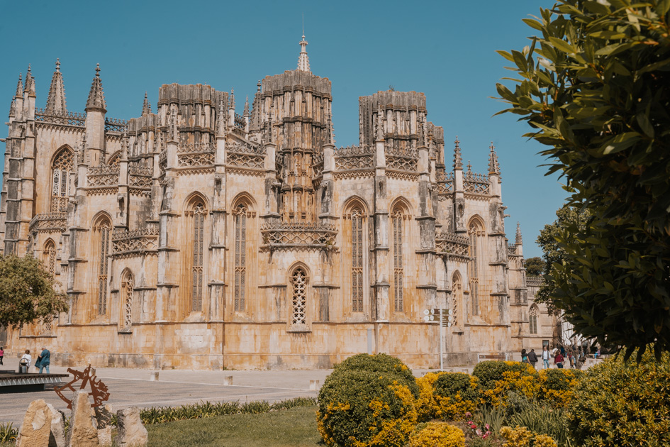 vast gothic Batalha Monastery stands behind a grassy area on a clear blue sky as one of the best day trips from Lisbon