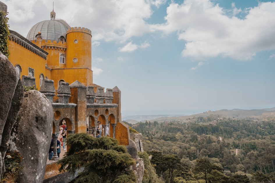an ornate yellow Pena Palace stands on the left overlooking the green coastline of Portugal, just 30 minutes travel to Lisbon tips