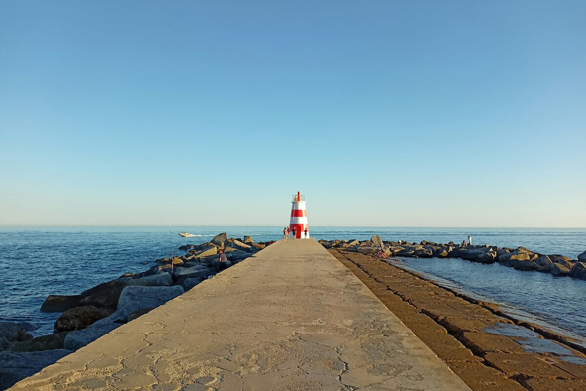 concrete peninsula pathway leads out to a red and white striped lighthouse along the coast of Portimao Algarve best towns