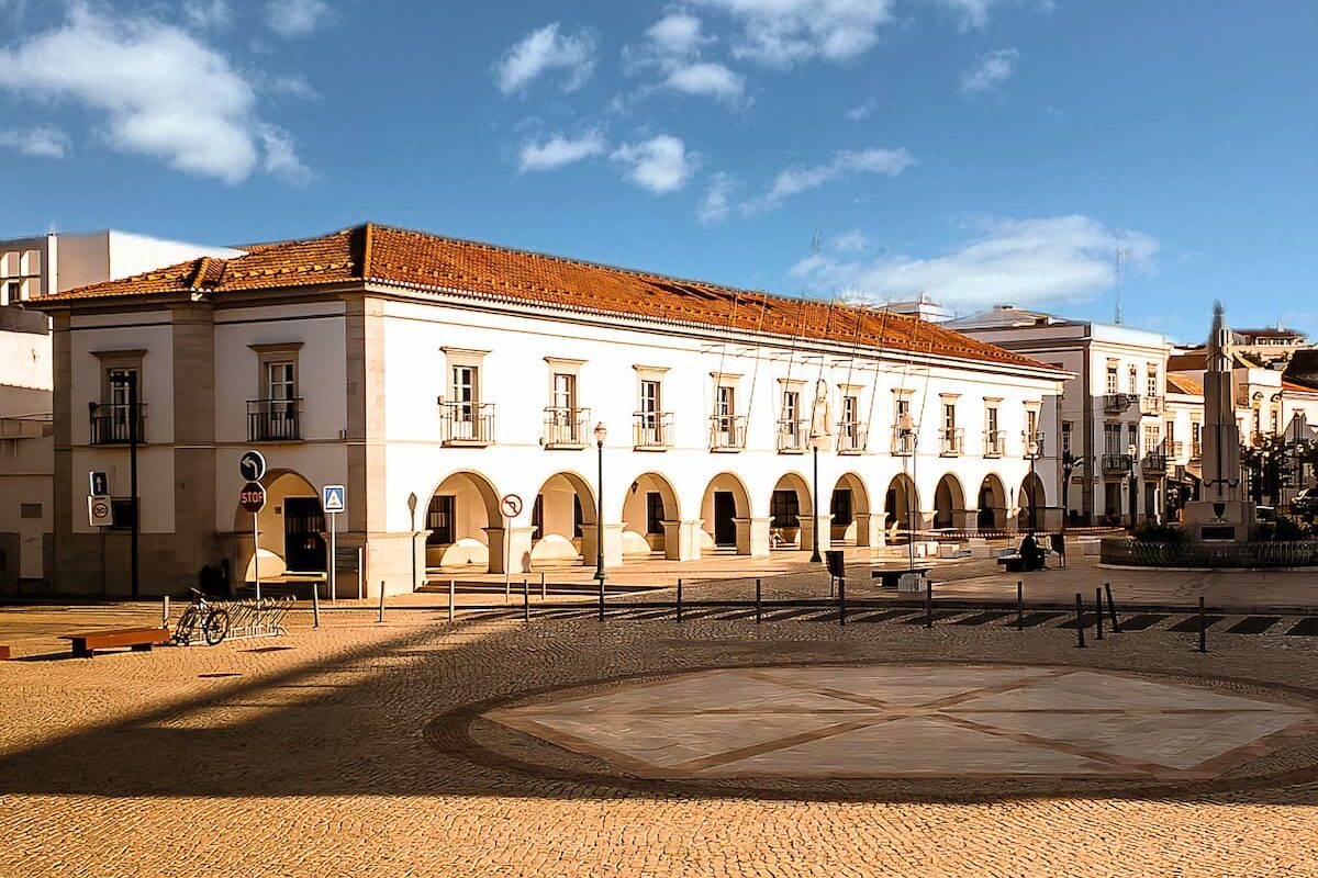 two story white building with arched pathway and red tiled roof sits behind the Tavira town square on a sunny day in Algarve where to stay