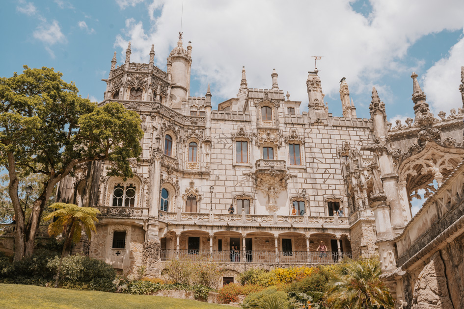 ornate stone castle with several towers sits behind greenery on a blue sky day in Sintra Portugal on Silver Coast where to stay for romantics and couples