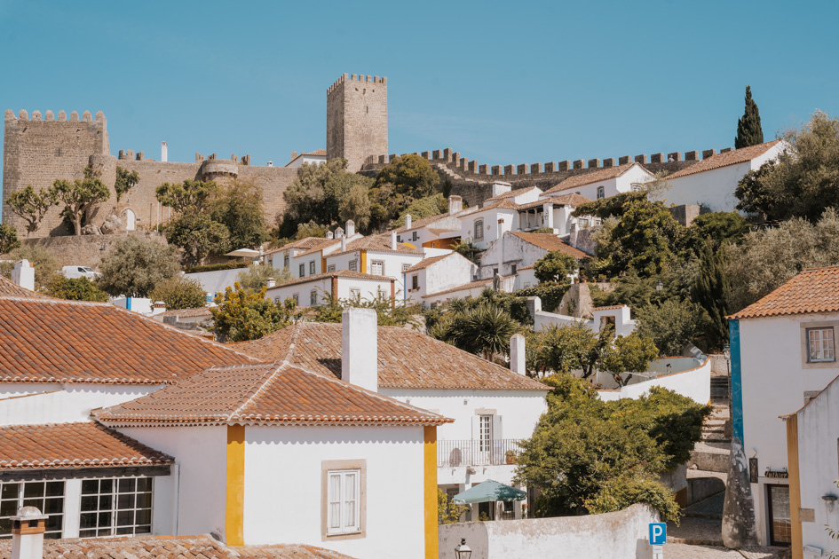 a grey stone wall surrounds Obidos with its white buildings, greenery and blue sky in Portugal Silver Coast town