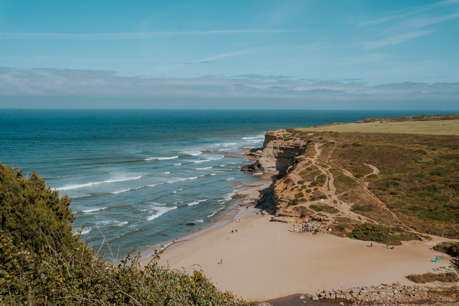 expansive sandy beach sits along a rugged green coastline with waves coming in from the Atlantic in a Portugal Silver coastal town