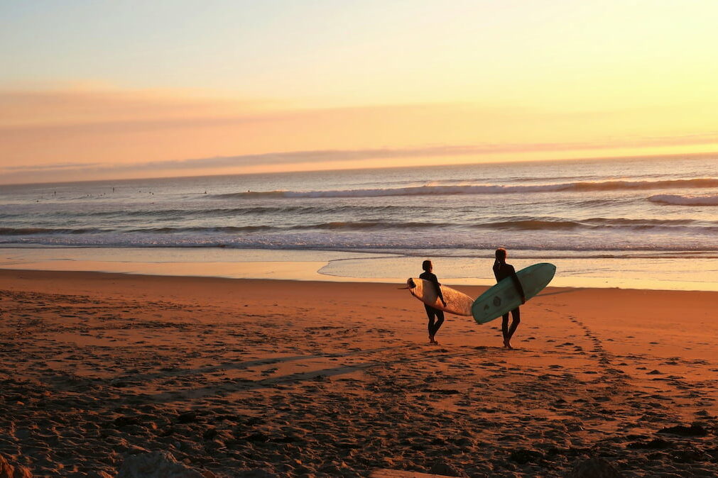 two surfers with surfboards stand on a beach at sunset in Figueira da Foz Portugal town