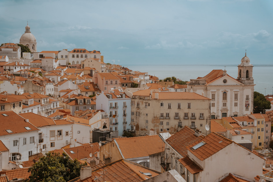 panoramic view over red tile roofed white buildings with the Tagus River in the background at one of Alfama's best viewpoints