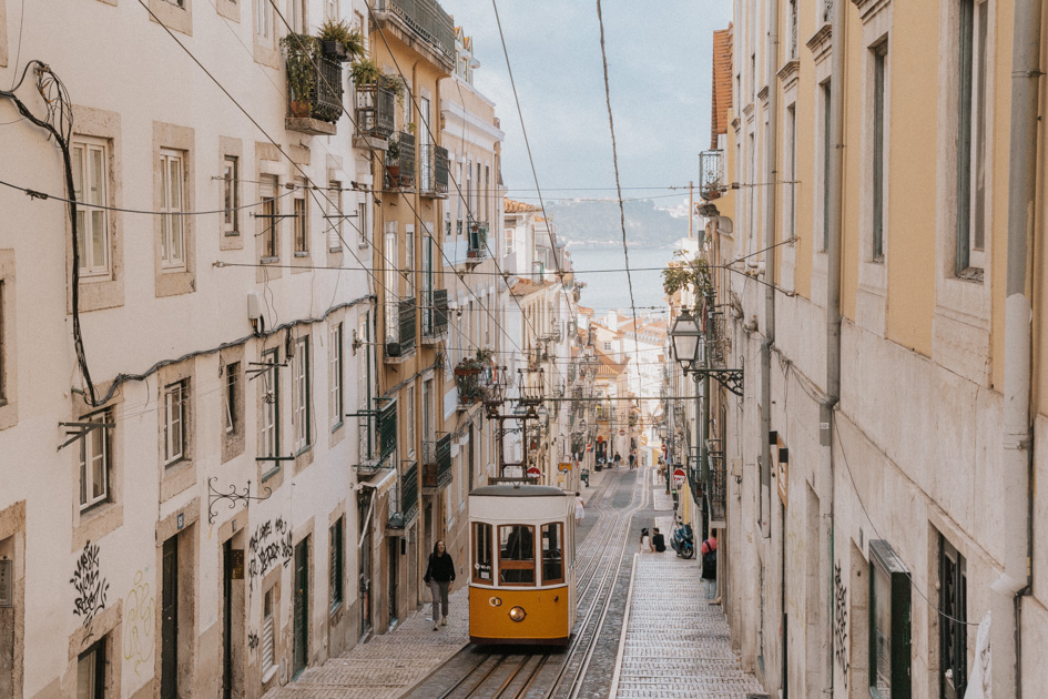 a historic yellow and white tram runs downhill on a track between tall white buildings in Chiado Lisbon things to see