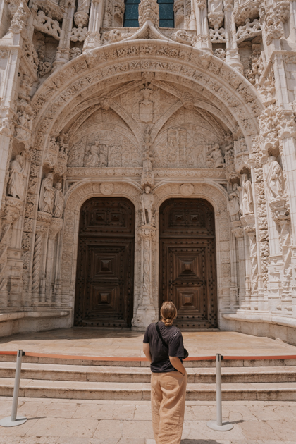 Haley Blackall wearing beige and black looks up at an ornate monastery doorway  in Lisbon for the first time