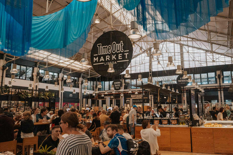 bustling indoor food market with large sign reading 'Time Out Market Lisboa' with blue fabric draping from the ceiling