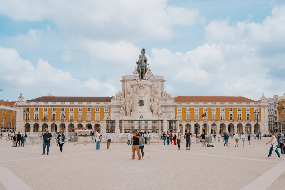 The placa do comercio with historic buildings and large monument on a partly cloudy day on a 1 day Lisbon itinerary