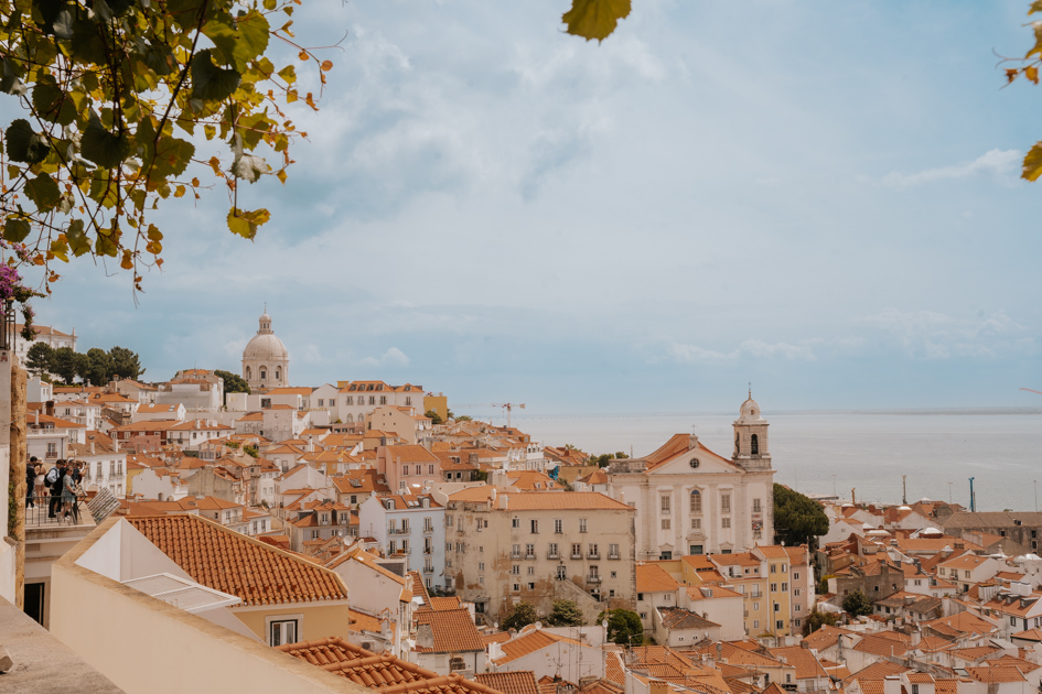 panoramic over red tiled white buildings descending down a hillside into the Tagus River beyond