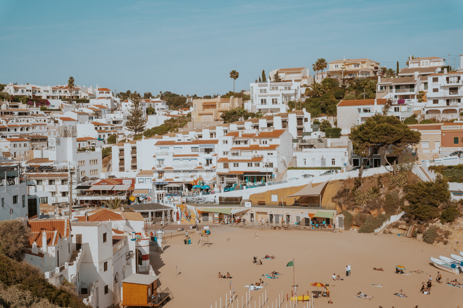 sandy beach sits at the base of a small Algarve town with whitewashed buildings and red roofs on a sunny day