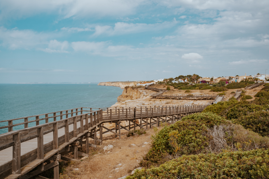 a wooden boardwalk meanders along a rugged coastline in Algarve Coast on a partly cloudy day