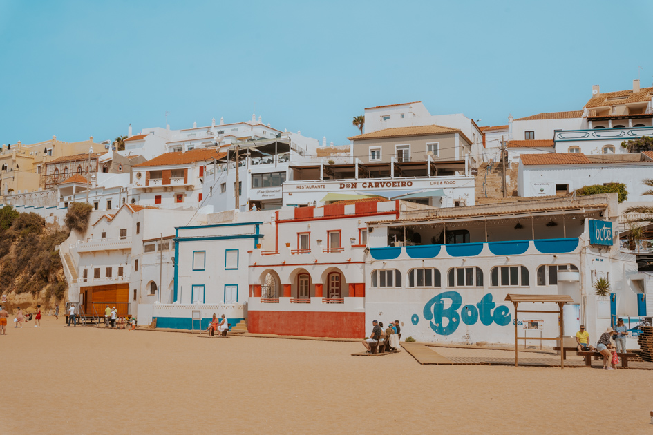 white, red and blue buildings line a golden sand beach in Carvoeiro which is the best Algarve town for beaches and boardwalks
