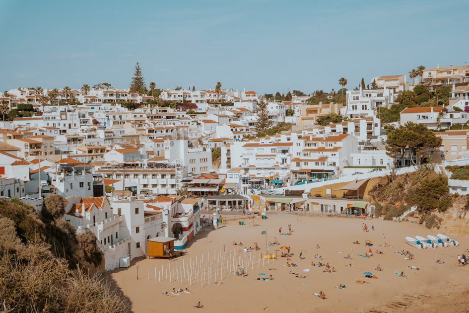 white buildings with red roofs sit back from a golden sandy beach with blue sky is where to stay in Algarve Portugal for families