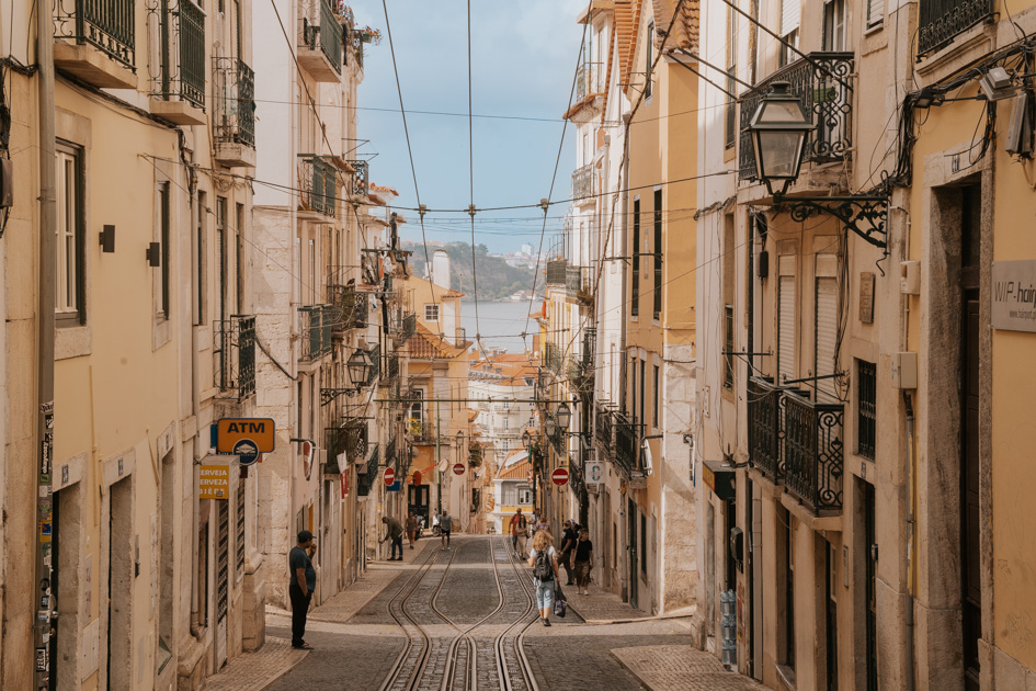 historic street leading downhill to the ocean in Lisbon with a man wearing black standing to the left