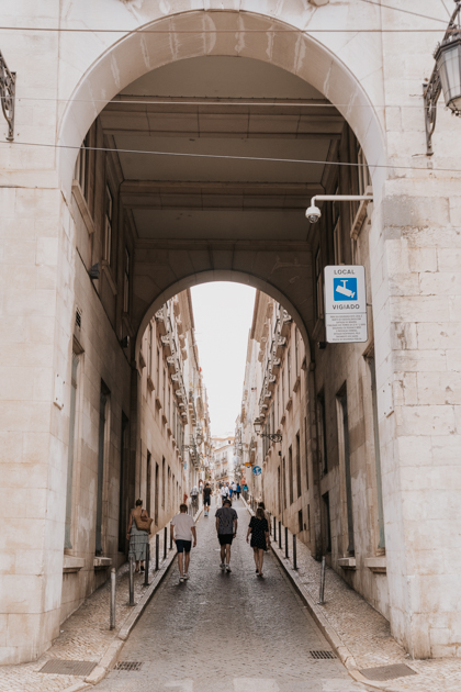 white stone arch leads to a bustling street in Bairro Alto Lisbon neighbourhood