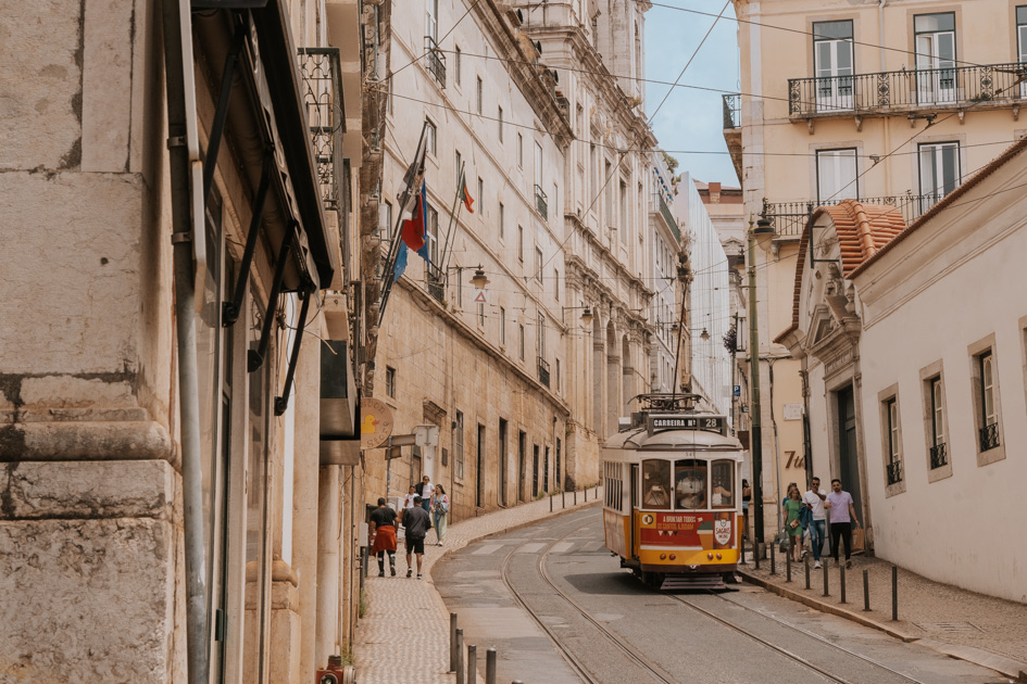 tram picks up passengers in between white stone buildings on a street that's ideal for where to stay in Lisbon Portugal for nightlife