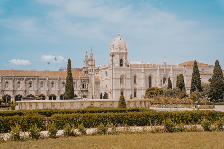white stone monastery sits behind a lush park on a sunny day in Belem which is a good location to stay in Lisbon for families