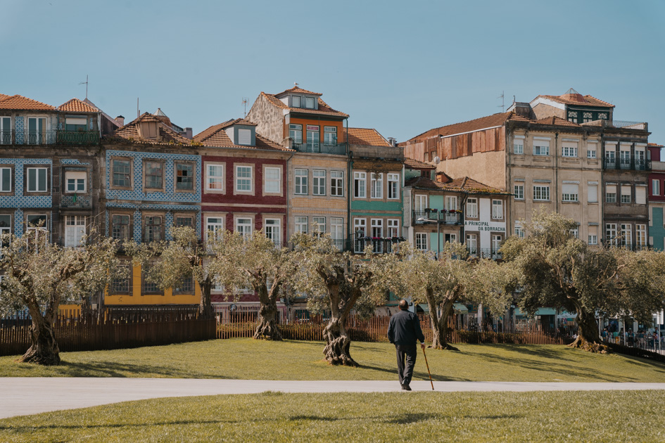 an elderly man walks with a cane along a concrete path in a green space with colourful buildings and blue sky in one of the best places to stay in Porto Portugal