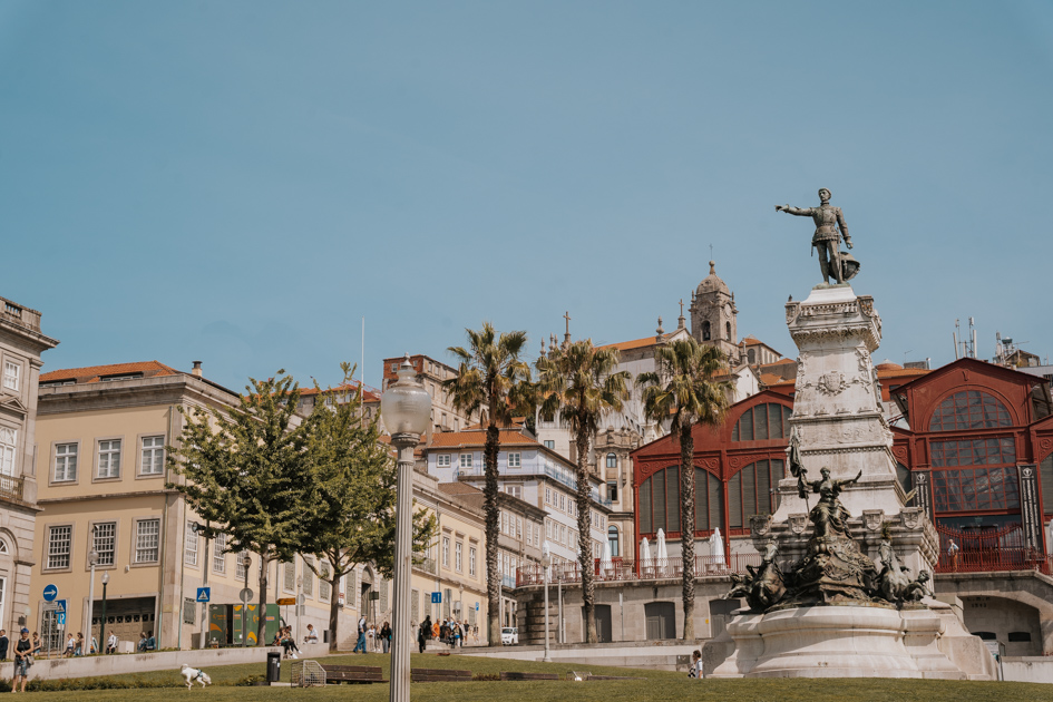statue of Dom Henrique in the middle of a green space with a restored red painted warehouse in the background on a clear day in Porto's neighbourhood of Ribeira