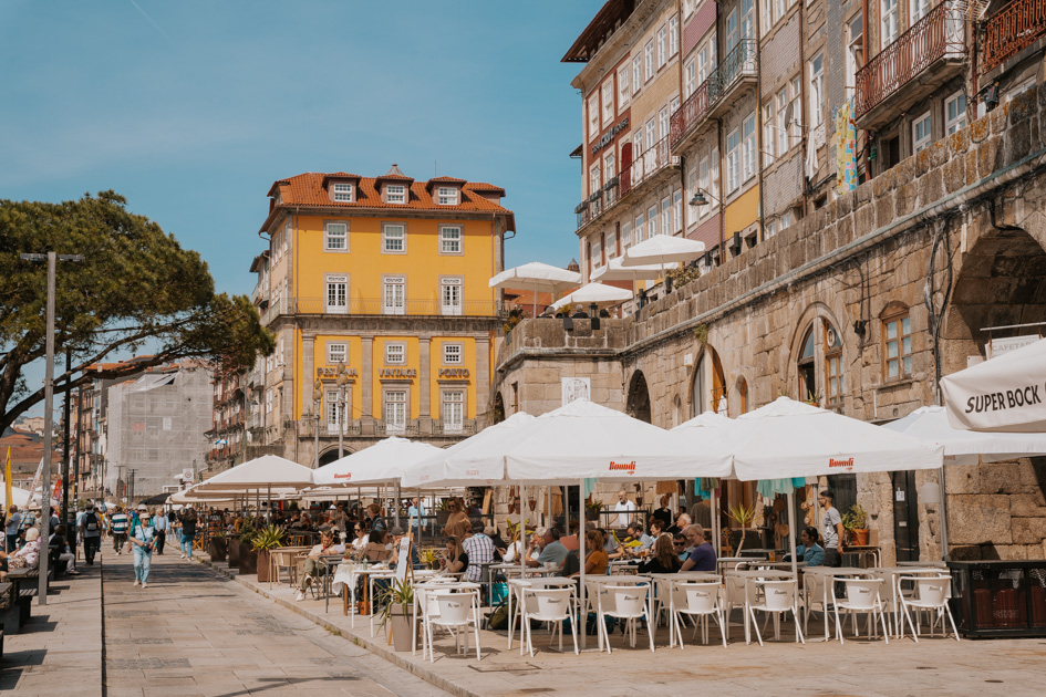 outdoor dining under white umbrellas in historic Ribeira with yellow building and blue sky in the distance in one of the best areas Porto has to offer
