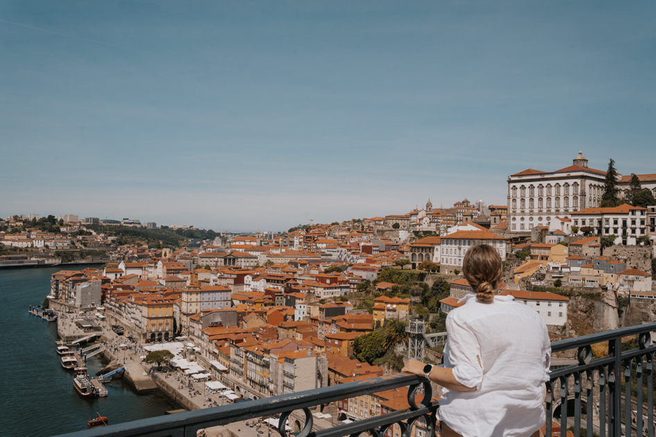 Woman wearing white shirt looks out from a bridge over Porto neighbourhoods and some of the best areas to stay in Porto Portugal on a sunny day