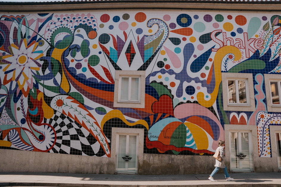 colourful graffitied wall in Cedofeita with a woman walking in front in the best area to stay for couples in Porto