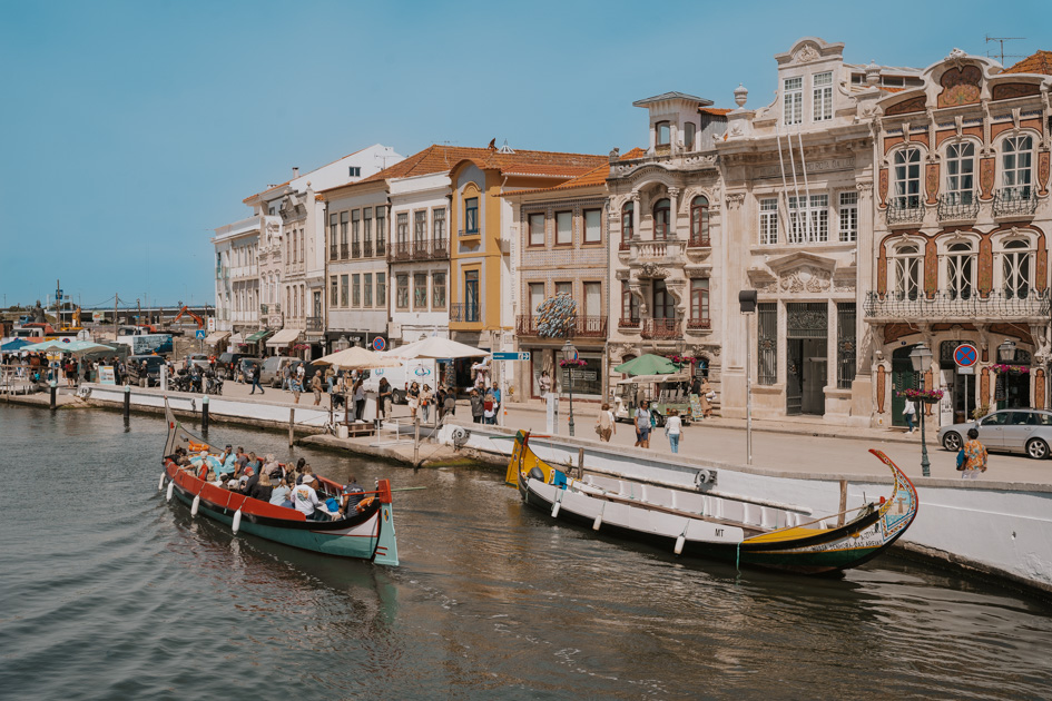 traditional colourful boats float on a canal in front of baroque buildings on a clear sunny day in one of the best places to stay on Silver Coast of Portugal