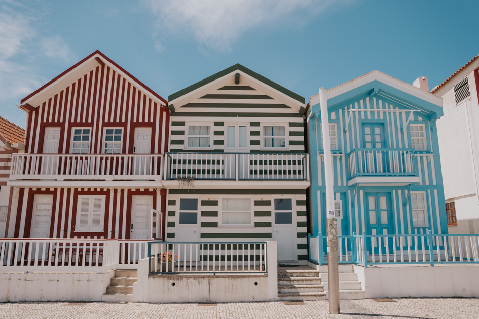 three two story houses each with either red and white strip, green and white strip or blue and white strip exteriors along a promenade on a sunny day in Costa Nova Portugal Silver Coast