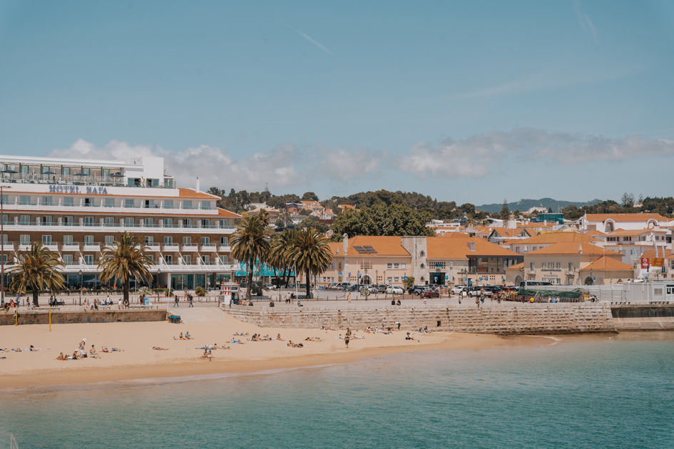 golden sandy beach lines a sophisticated coastline with blue waters and multi story hotel in Cascais Portugal town
