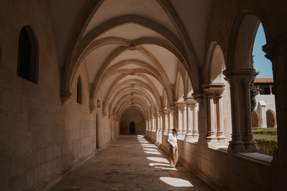 Haley Blackall stands in the light between stone arched openings in a long hallway in Batalha where to stay in Portugal Silver Coast for architecture 